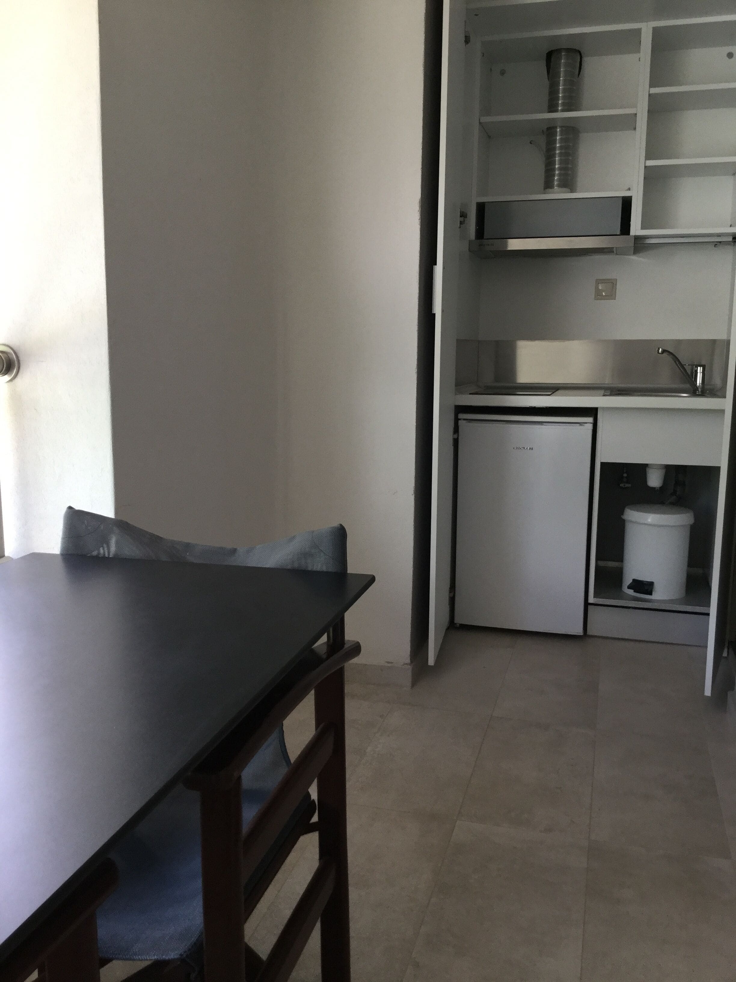 A compact kitchen with a refrigerator, sink, and storage shelves.