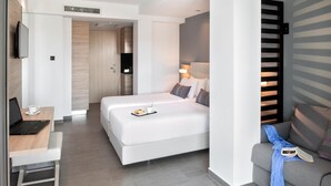 Quarto de hotel moderno com cama, escrivaninha com laptop, televisão e sofá.