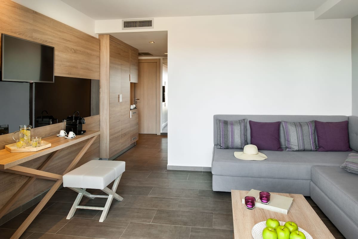 Een moderne woonkamer met een grijze bank, een houten salontafel met appels, een witte bank en een aan de muur bevestigde televisie.