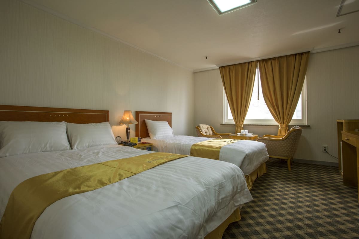 Une chambre d’hôtel avec deux lits, un bureau, une chaise et une fenêtre avec des rideaux.