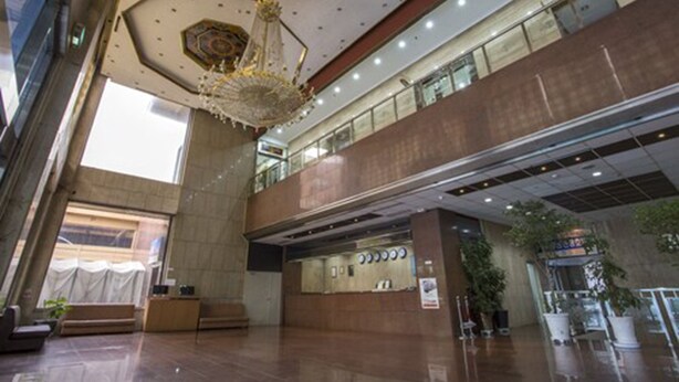 Un hall d’entrée spacieux, doté d’un plafond haut, d’un lustre central et d’un comptoir de réception.
