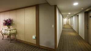 Un couloir d’hôtel avec un tapis à motifs, un vase décoratif rempli de fleurs et une porte coulissante traditionnelle.