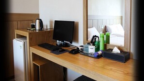 Une chambre d’hôtel avec un bureau en bois, un ordinateur, une machine à café, des articles de toilette et un lit avec du linge de maison blanc.