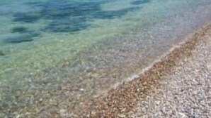 Una playa despejada con piedras y un promontorio rocoso en el agua.