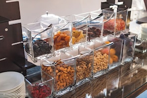 A buffet with clear glass containers holding various nuts, dried fruits, and other snacks.