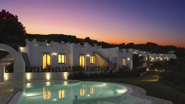 Un resort con piscina, un edificio blanco de ventanas arqueadas y una puesta de sol al fondo.
