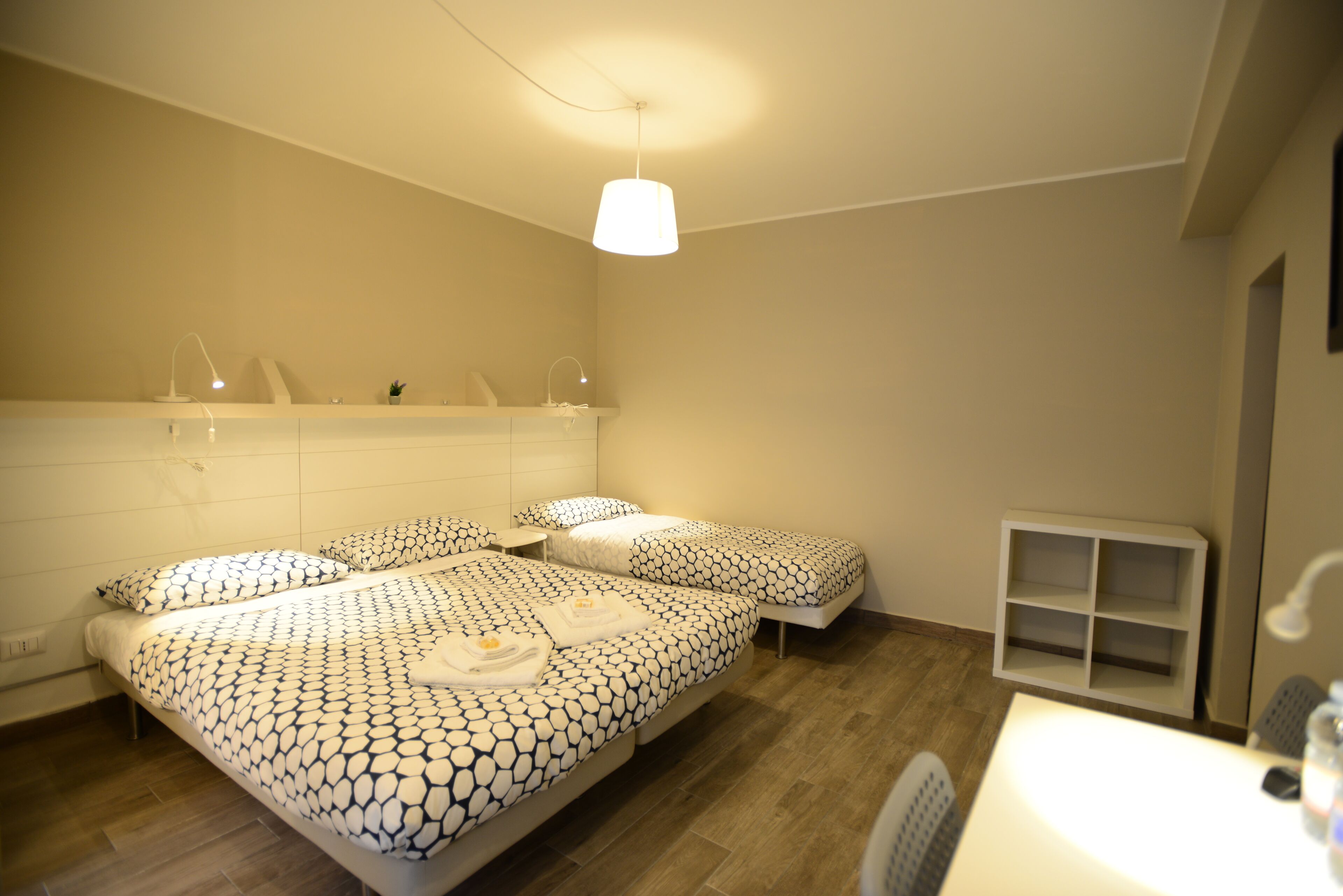 A hotel room with two beds, a small desk, a mirror, and a shelf with toiletries.