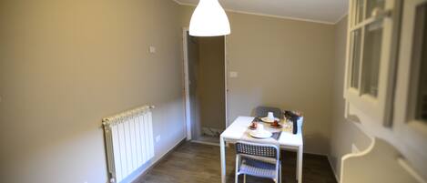A room with a dining table, chairs, a hanging light fixture, and a radiator.