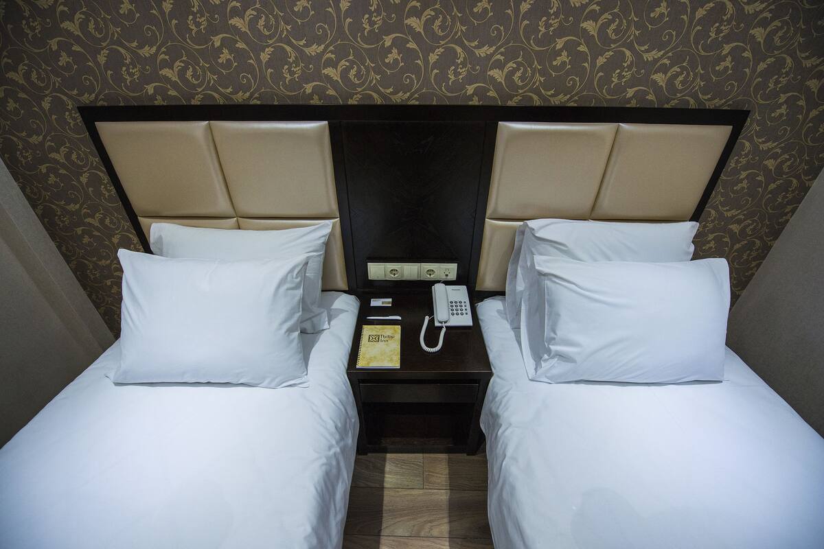 Une chambre d’hôtel avec deux lits, une table de chevet avec un téléphone et un bloc-notes, et un papier peint à motifs.