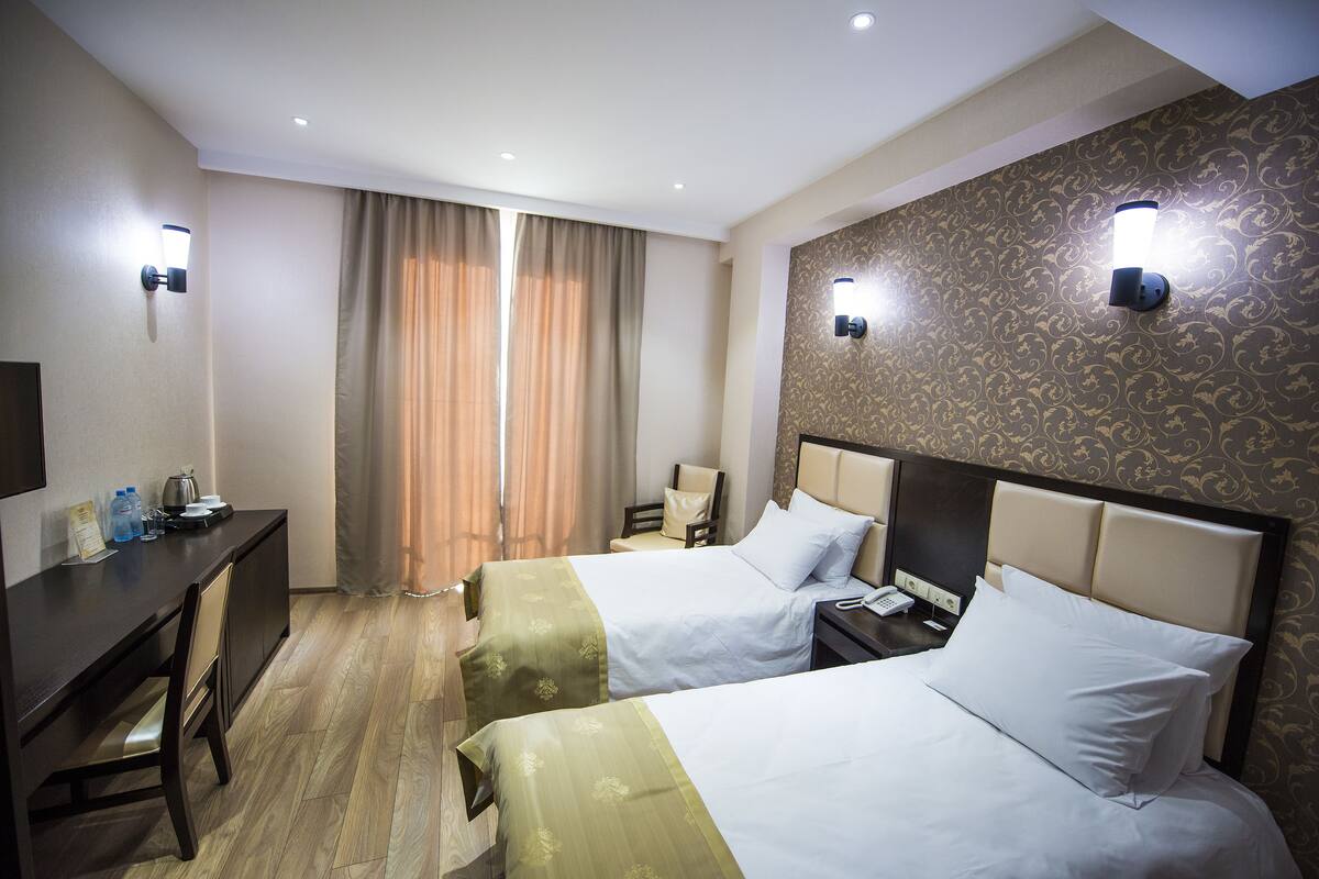 Une chambre d’hôtel avec deux lits, un bureau, une chaise et une petite table avec une lampe.
