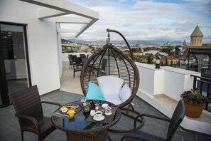 A balcony with a hanging chair, a table with breakfast items, and a potted plant.