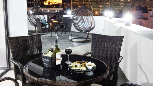 A rooftop dining area with wicker furniture, a table set with a bottle of wine, glasses, and a plate of food. - Tbilisi Inn (Tbilisi)