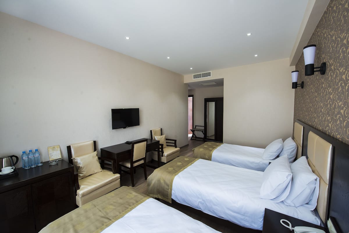 Une chambre d’hôtel avec deux lits, un bureau, une chaise, une télévision et une petite table avec une bouilloire et des bouteilles d’eau.