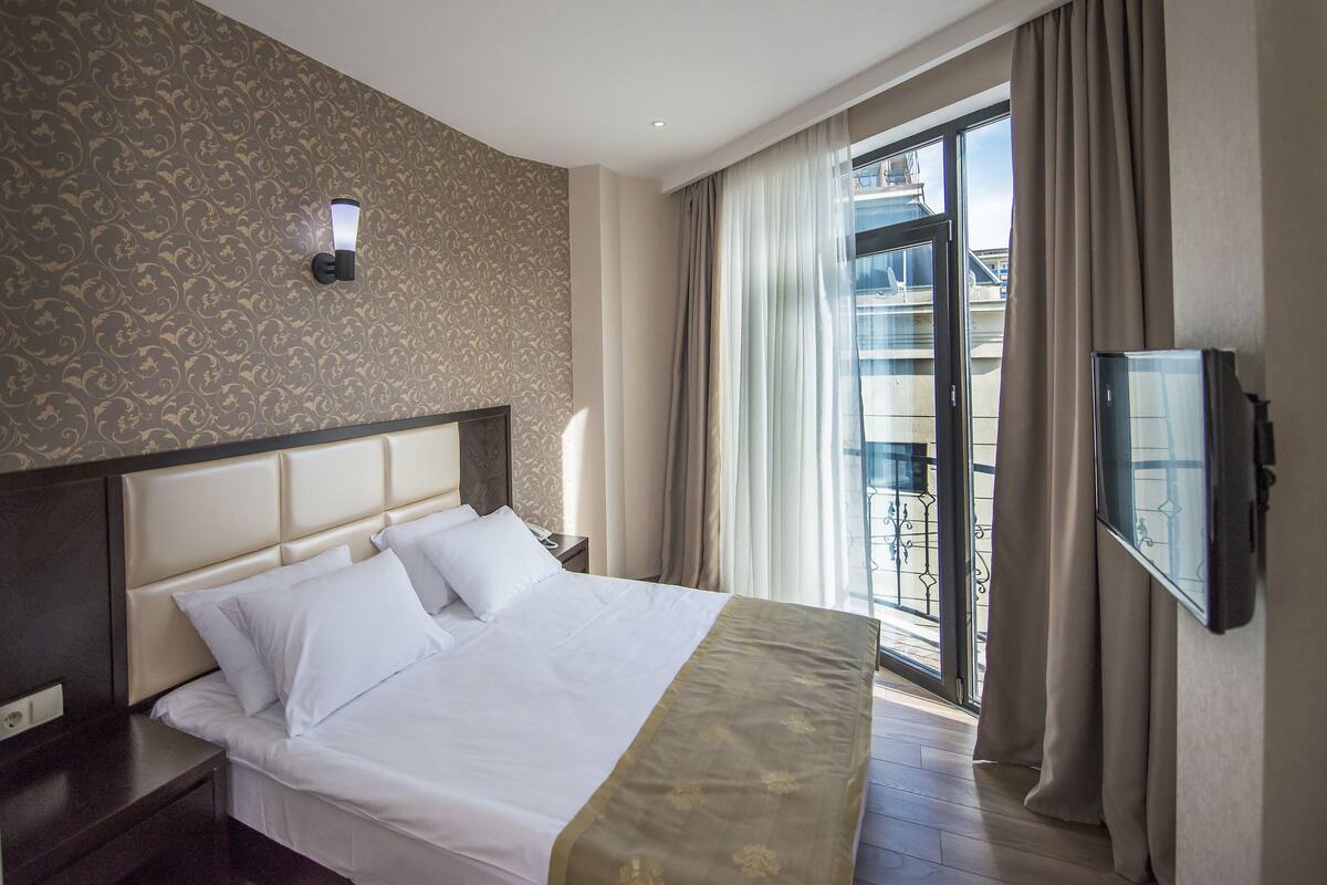 Une chambre d’hôtel avec un grand lit, une table de chevet, un téléviseur fixé au mur et un balcon offrant une vue sur la ville.