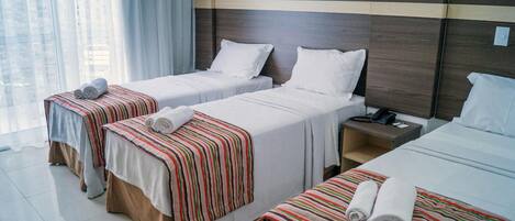 Habitación de hotel con dos camas individuales, cada una con una manta a rayas y toallas enrolladas. Hay una mesita de noche con un teléfono y una lámpara.