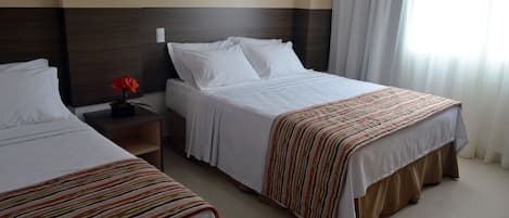 A hotel room with two beds, a nightstand with a vase of flowers, and a large window with curtains.