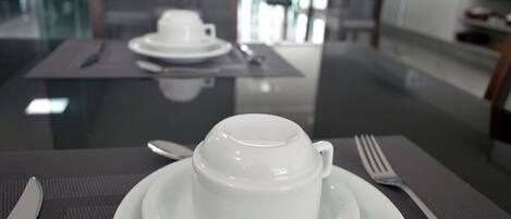 A dining table with a white cup and saucer, a fork, and a knife.