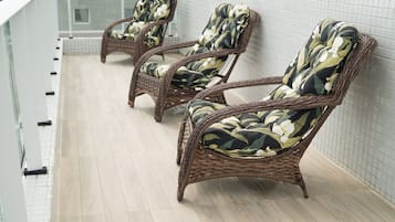 Poltrone da relax in vimini con rivestimenti floreali su un balcone piastrellato.
