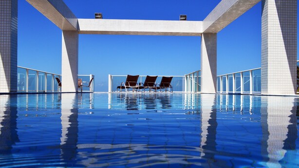 A clear blue pool with a tiled deck and lounge chairs. - Val Atlantic Hotel (João Pessoa)