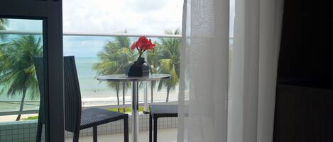 Un balcón con mesa y sillas, con vista a una playa con palmeras y el océano.