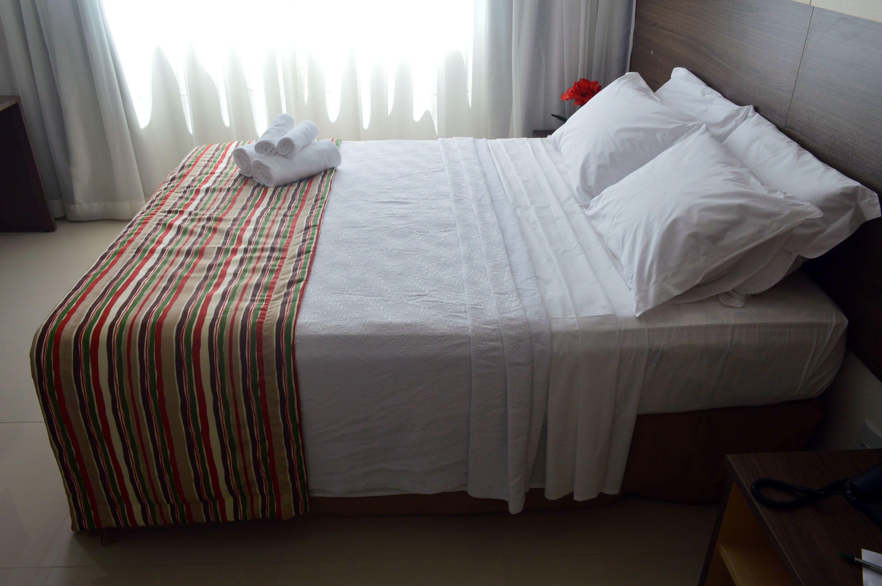 A neatly made bed with white linens, striped bedspread, and pillows.