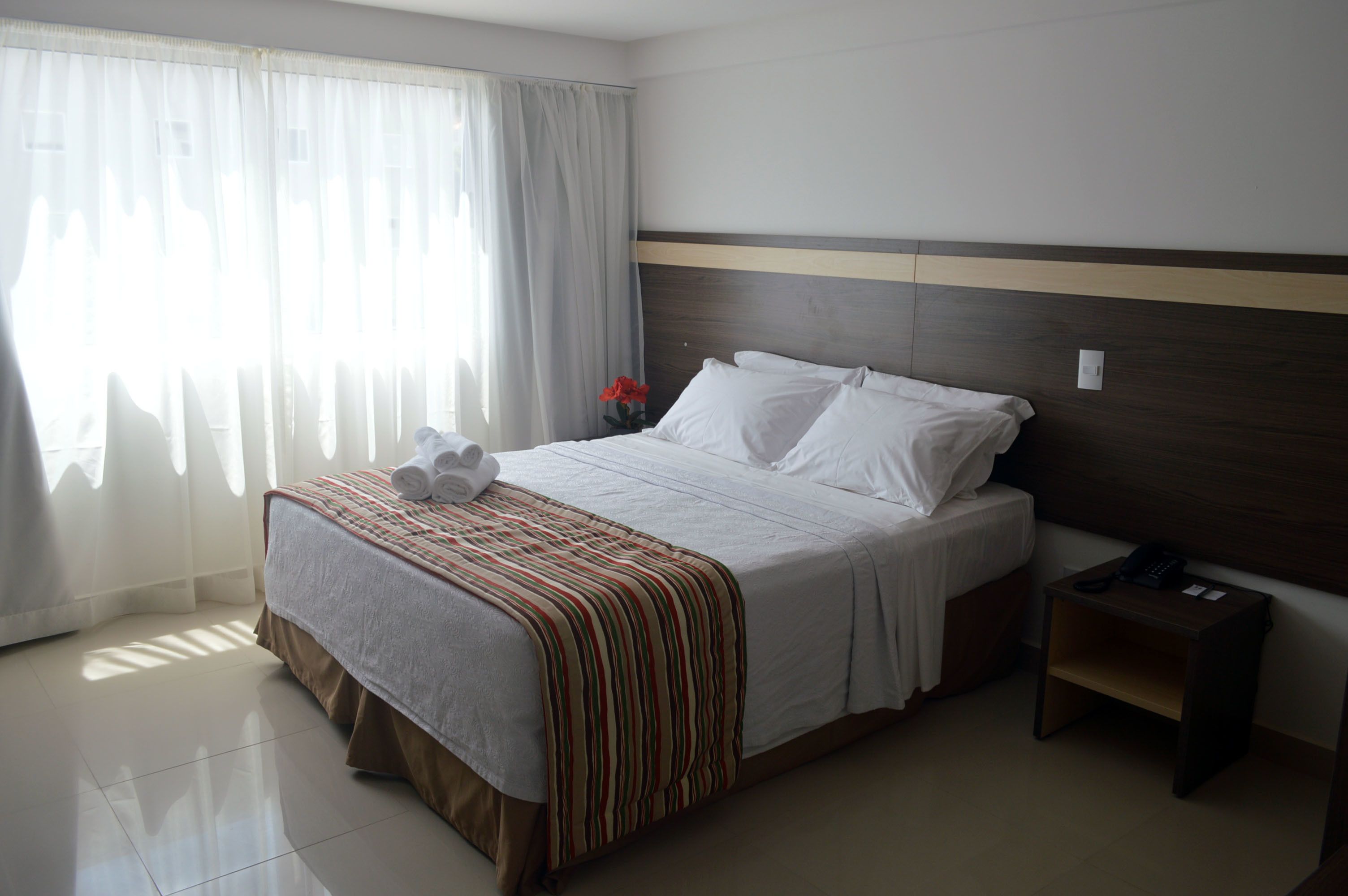 A hotel room with a large bed, a nightstand, a telephone, and a window with curtains.