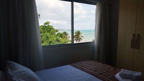 A hotel room with a bed, a window with a view of the beach and palm trees, and a wooden wardrobe. - Val Atlantic Hotel (João Pessoa)