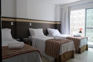 A hotel room with three beds, a large window with a view, and a small table with a vase of flowers.