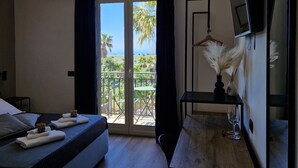 Habitación de hotel con cama, escritorio, silla, televisión y balcón con vista al mar.