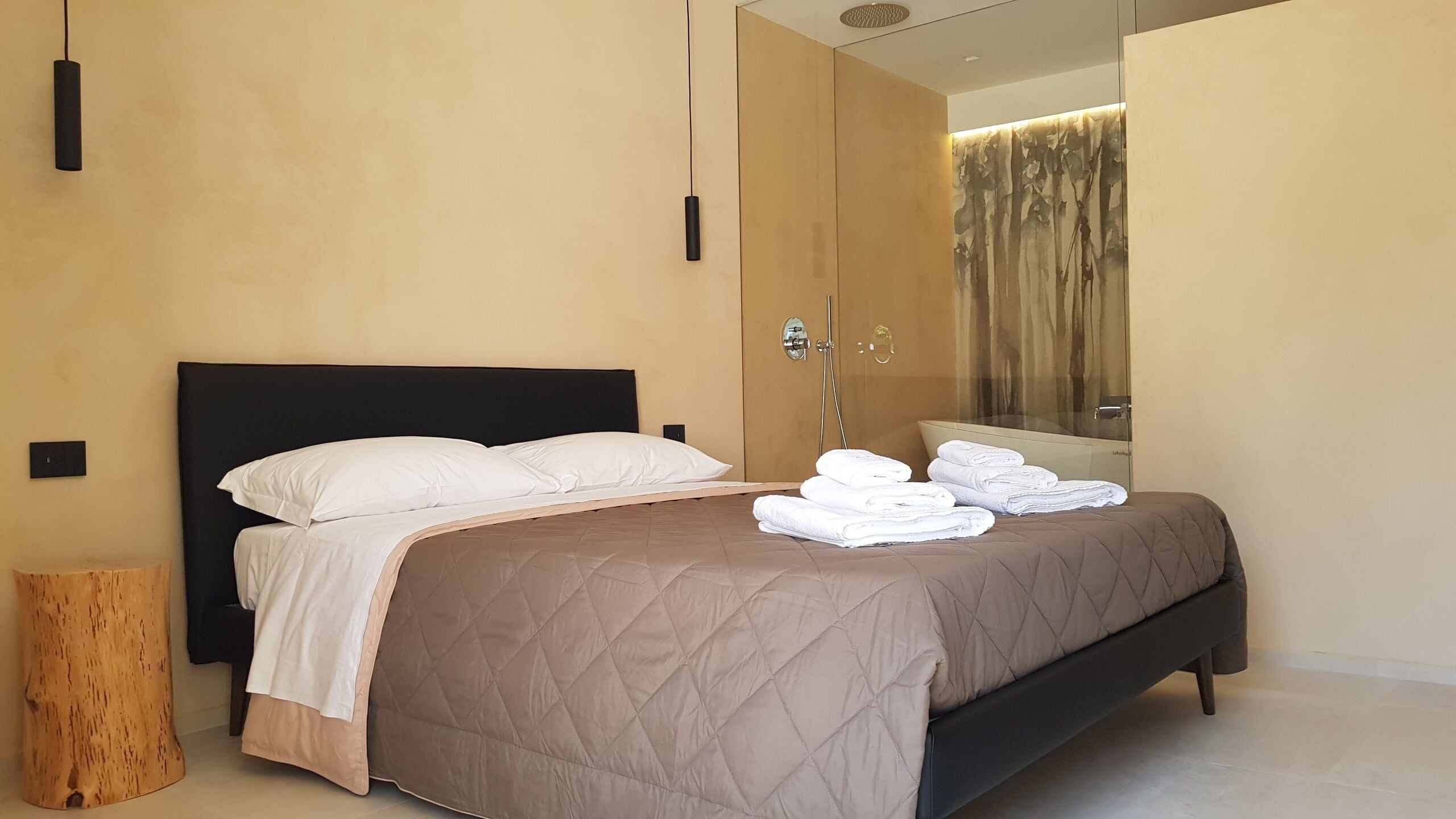 Una habitación de hotel moderna con una cama grande, una mesita de noche de madera, un espejo y un área de ducha.