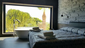 Un dormitorio moderno con un ventanal grande, una bañera y una cama con toallas.