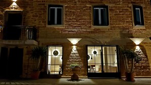 Un edificio de piedra con varias ventanas y puertas, plantas en macetas y un balcón.
