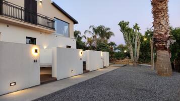 A modern house with a balcony, a gravel driveway, and a palm tree.