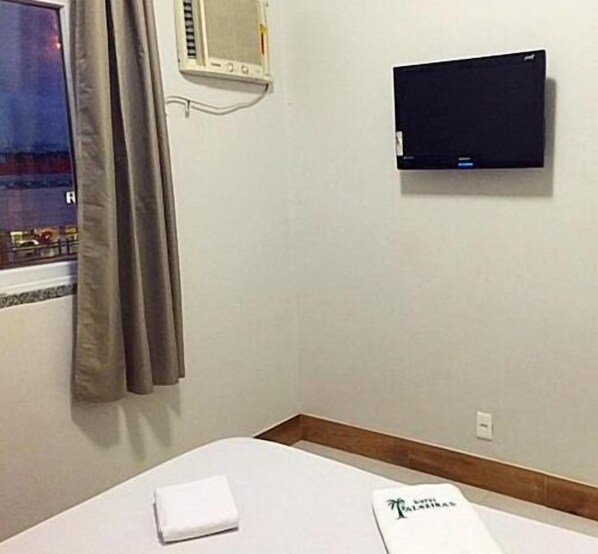 Habitación de hotel con cama, televisor montado en la pared, ventana con cortinas y una toalla sobre la cama.