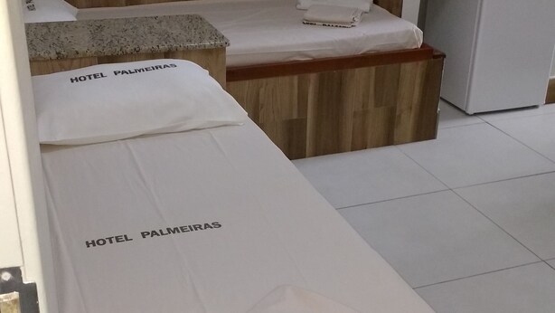 Habitación de hotel con dos camas, cada una con una colcha blanca y una toalla con el nombre del hotel. Se observa un cabecero de madera, un refrigerador pequeño y un microondas sobre el lavamanos.