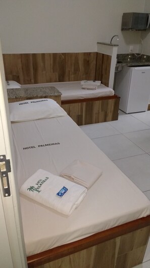 A hotel room with two beds, each with a white bedspread and a towel with the hotel name. There is a wooden headboard, a small refrigerator, and a microwave above the sink.