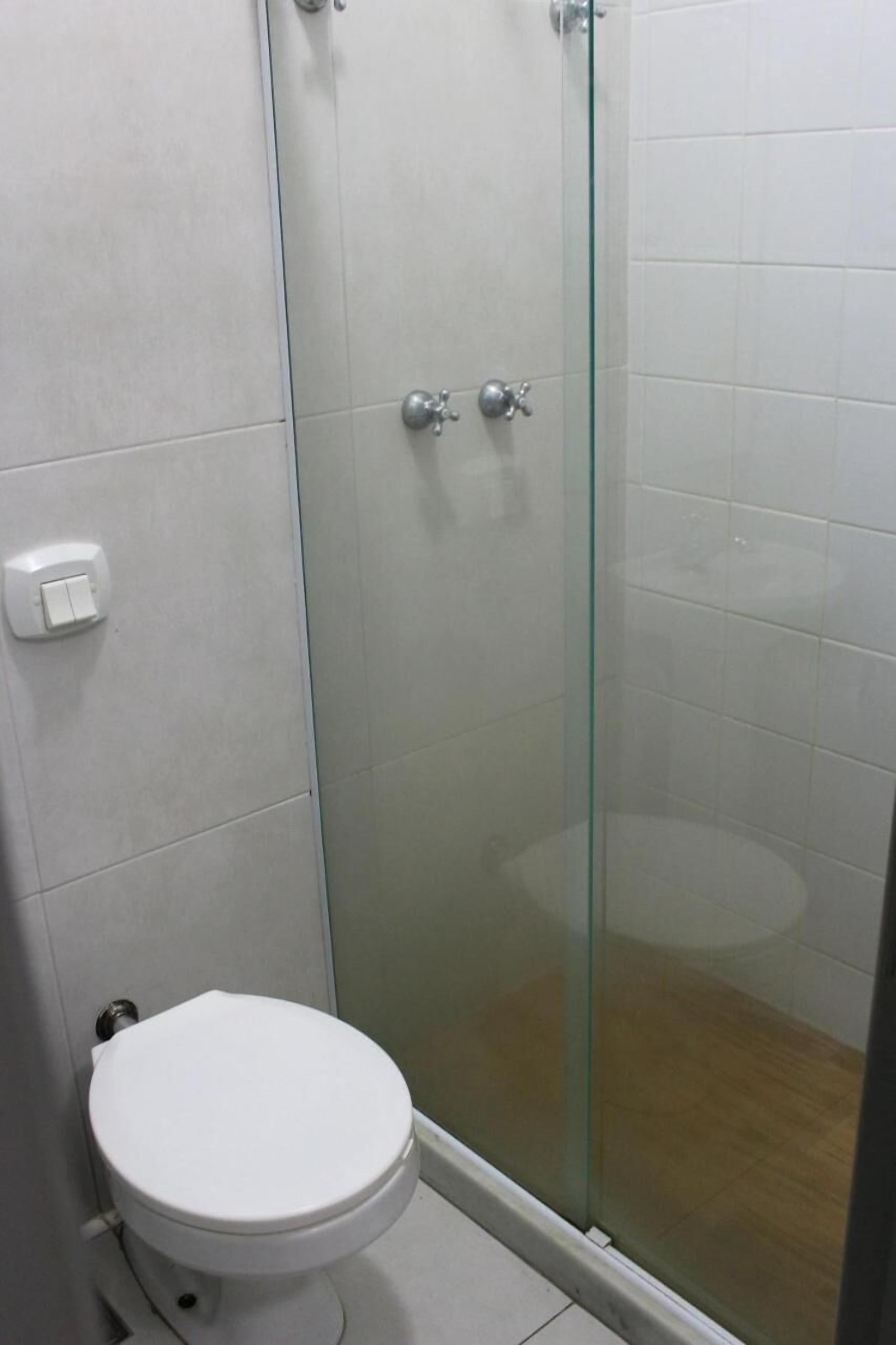 A bathroom with a toilet, a glass-enclosed shower, and a white tiled wall.