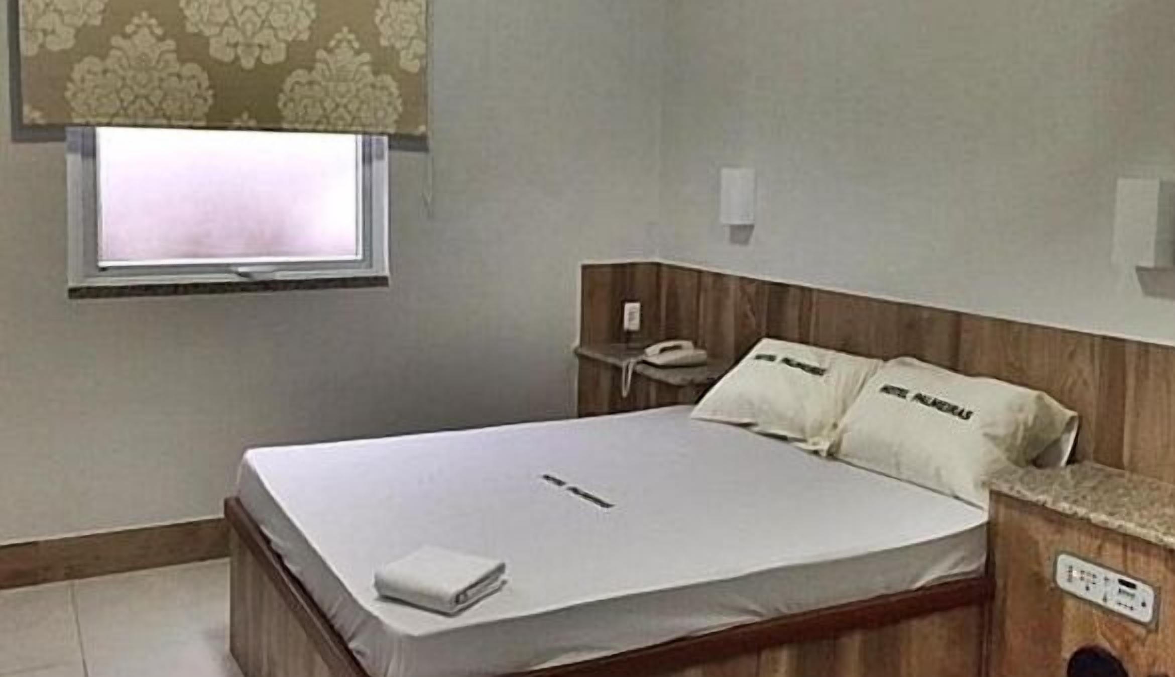 A single bed with a wooden headboard, a bedside table with a phone, and a window with a patterned curtain.