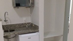 Una pequeña cocina americana equipada con microondas, lavamanos y refrigerador.
