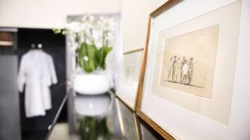 Ein Flur mit einem gerahmten Skizze an der Wand, einem weißen Kleid an einem Kleiderständer und einer Vase mit weißen Blumen.