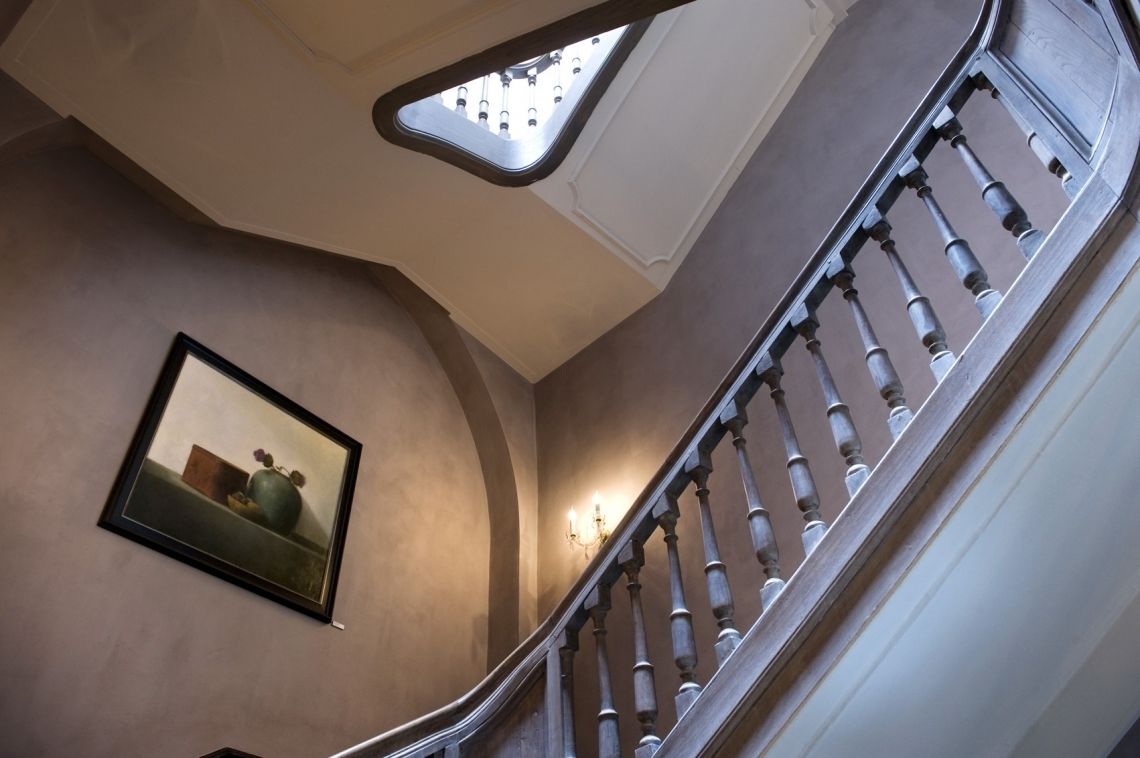 Una escalera curva con barandilla y balaustres, una obra de arte enmarcada en la pared y un tragaluz arriba.