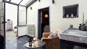 Um interior moderno com um pátio envidraçado, uma mesa redonda com um copo de cerveja, uma poltrona confortável e uma bancada de pedra.