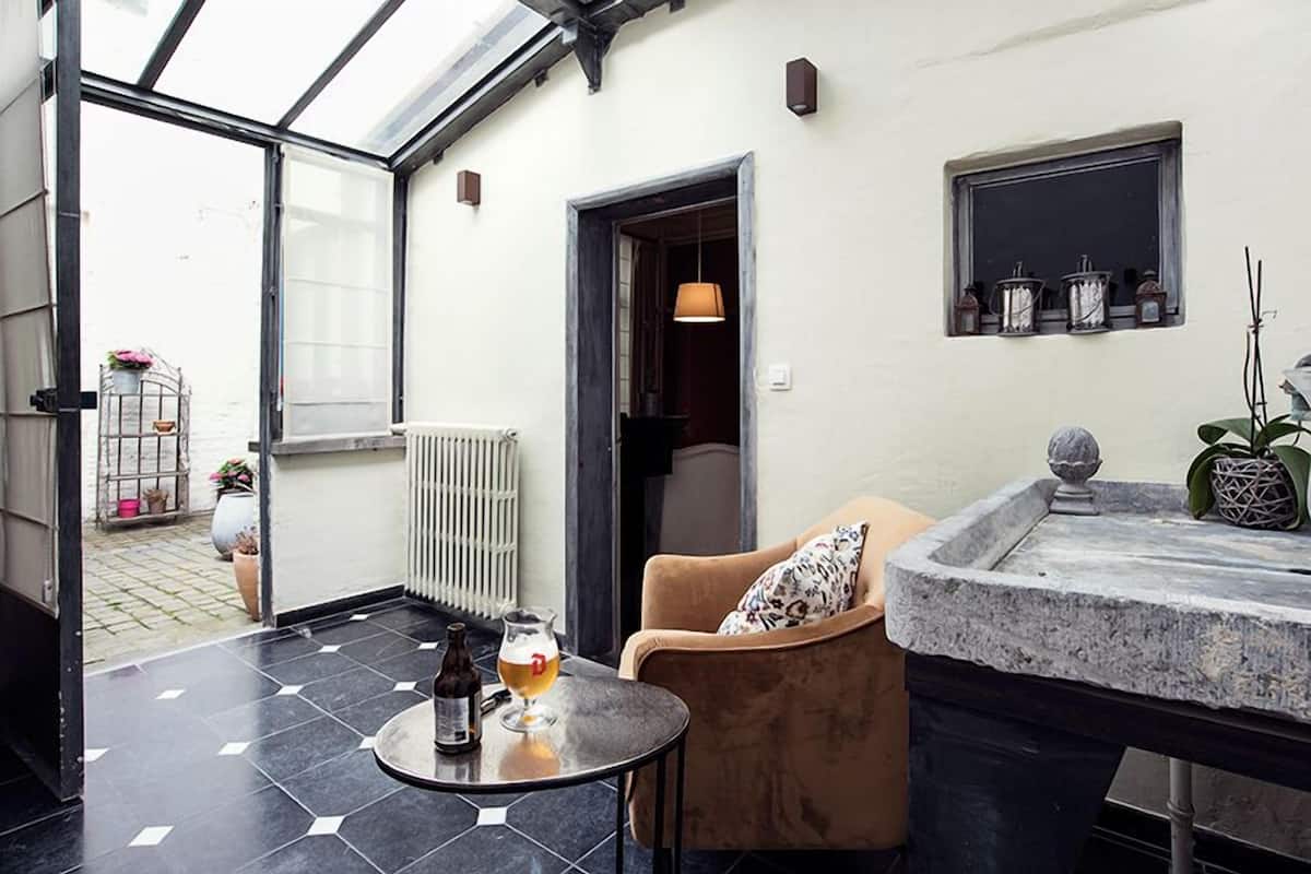 Un intérieur moderne avec un patio fermé par des baies vitrées, une table ronde avec un verre de bière, un fauteuil confortable et un comptoir en pierre.