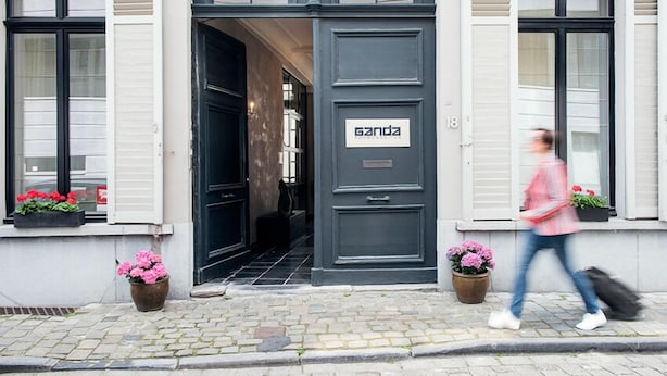 Entrada de um edifício com uma porta preta, uma placa com a inscrição 'ganda' e vasos de plantas de ambos os lados.