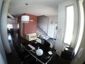 Uma sala de estar moderna com um sofá, uma mesa de jantar com cadeiras, uma escada e um grande janelão.