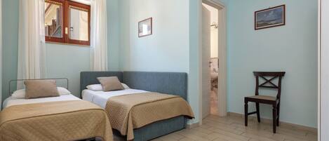 A bedroom with two beds, a wooden chair, and a bathroom visible through an open door.