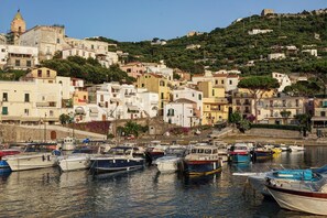 Une ville côtière où des bateaux sont amarrés dans le port, des bâtiments sont construits sur une colline et une tour imposante se dresse.