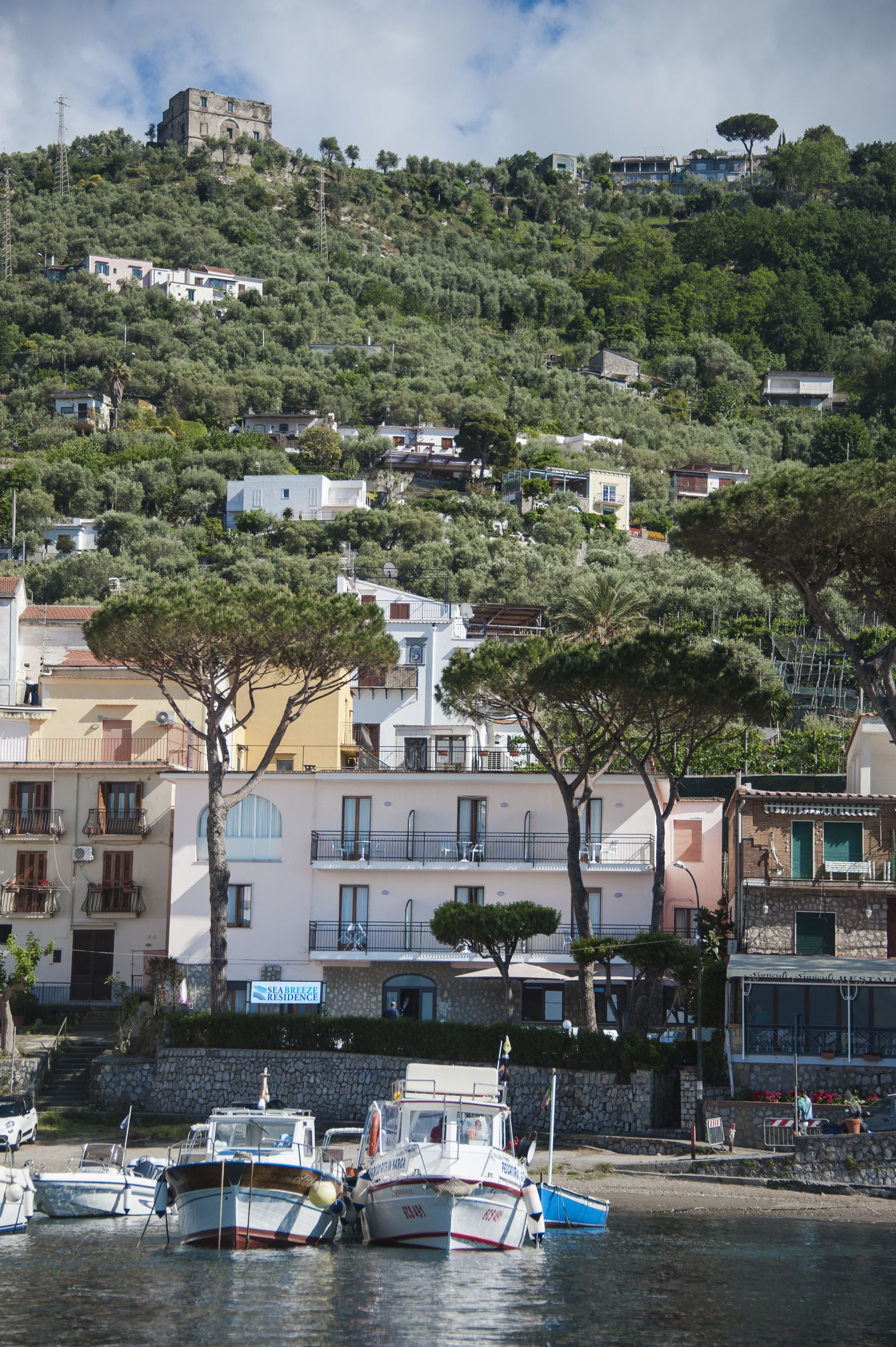 Une ville côtière avec des bâtiments construits sur une colline, un port de plaisance avec des bateaux et une tour imposante qui domine la colline.