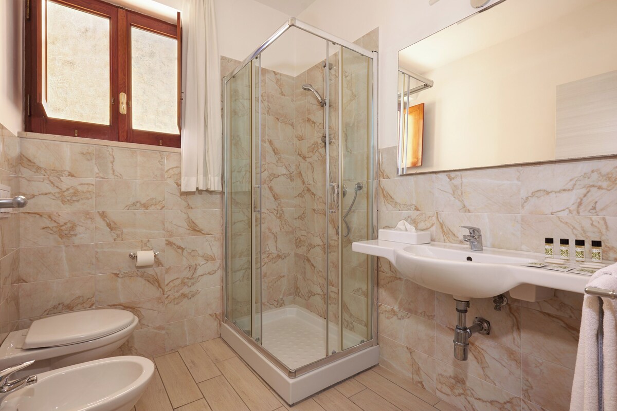 A bathroom with a glass-enclosed shower, a toilet, a sink, and a mirror.