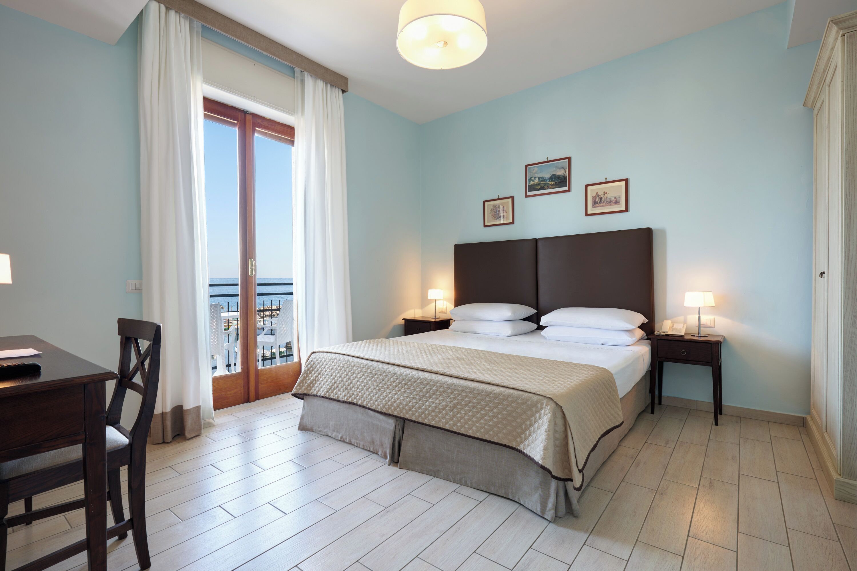A hotel room with a bed, bedside tables, a desk, and a chair.